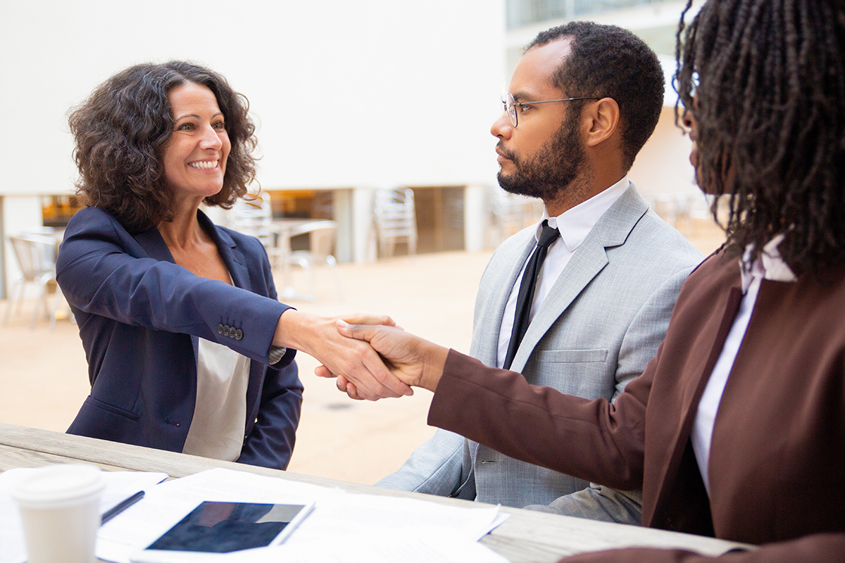 Applicant greeting HR manager at job interview. Business man and women sitting at table in outdoor cafe and shaking hands. Business meeting and handshake concept